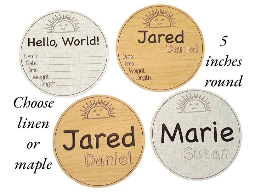 Newborn name and stats wooden round signs. Choose from linen or maple wood color options. Cute sun at the top, smiling. Hello world or name and birth stat area engraved. From Art by Iceberg.