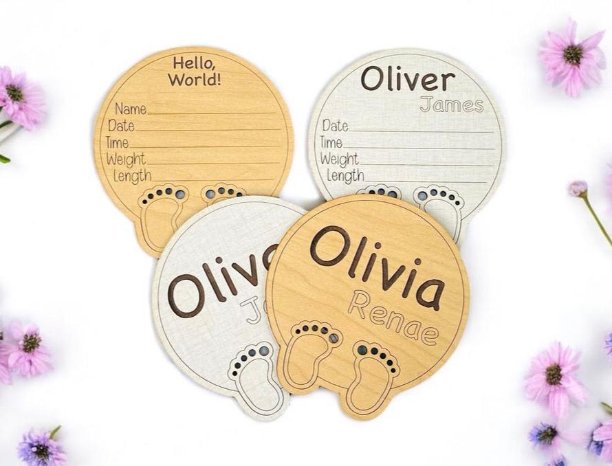 Personalized baby birth announcement sign. Round with Hello, World engraved at the top. Cute baby feet outline and laser cut toes at the bottom. Area to add the newborn name and birth stats. From Art by Iceberg.