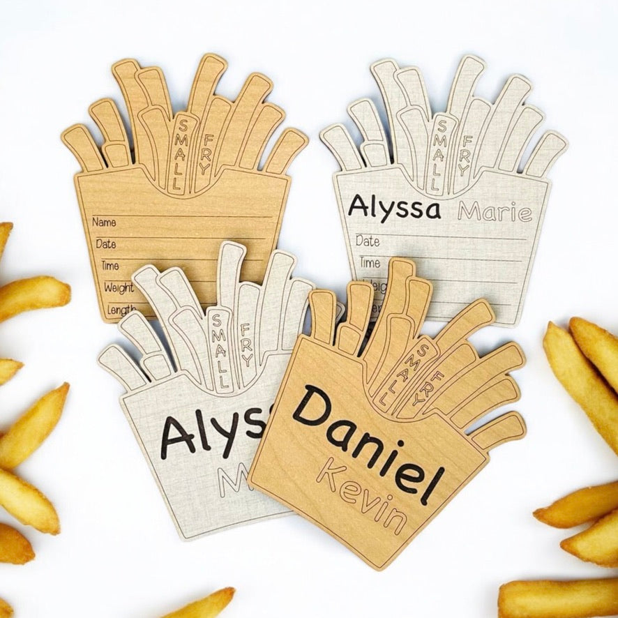 Baby birth announcement sign with a French fry fast food theme. Wood shaped like a container of fries. Choose from linen or maple wood color options. Fill in the newborn name and birth stats with a pen or marker. From Art by Iceberg.